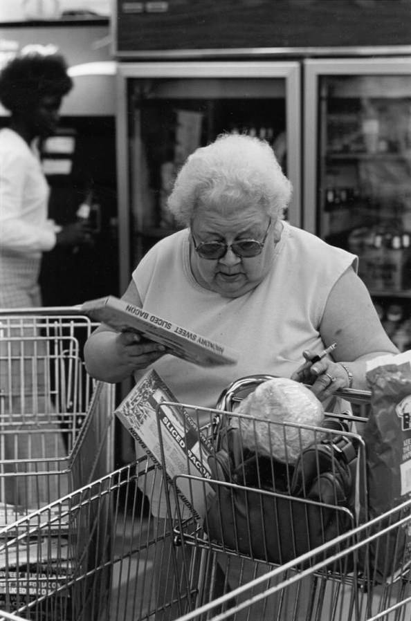 Woman putting bacon in grocery cart, 1980