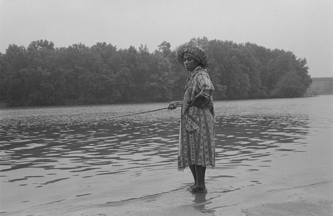Woman in housecoat fishing at Flint River, 1979 June