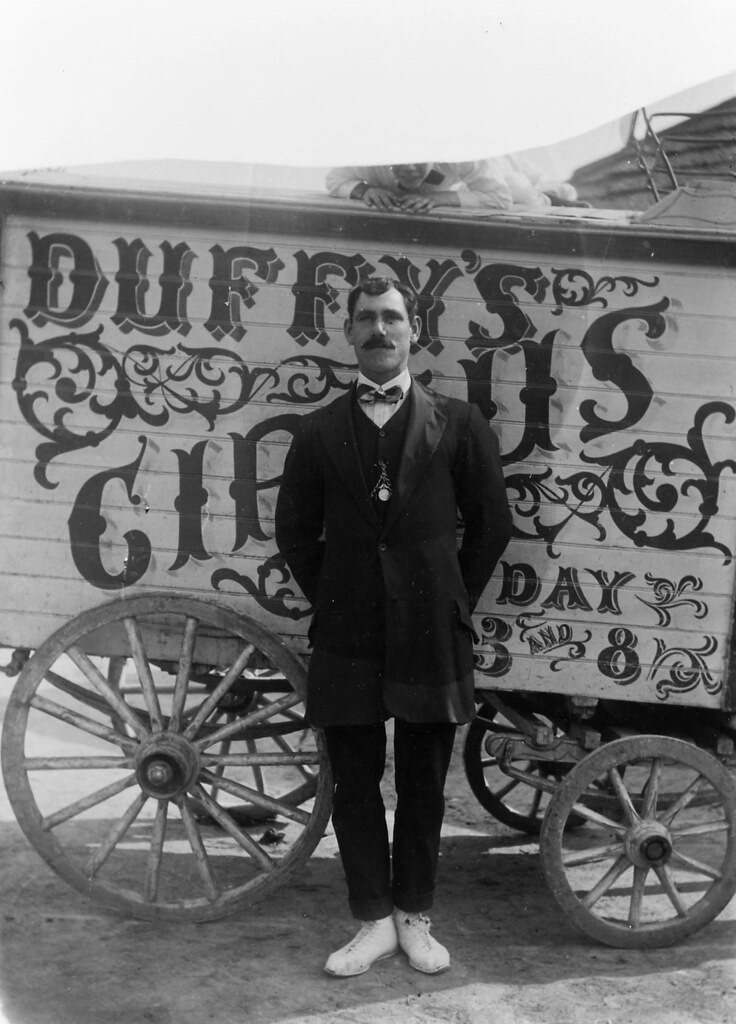 Duffy's Circus, man standing in front of a wagon labelled, 'Duffy's Circus', 1911.
