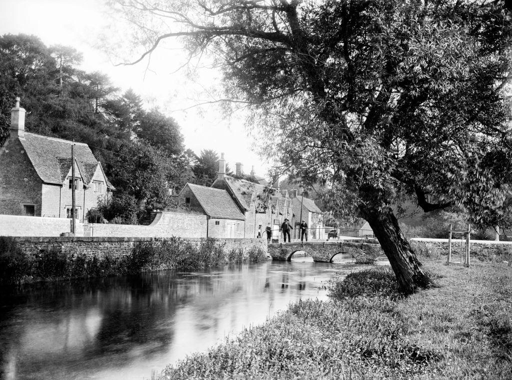 Bibury, Gloucestershire, 1906. View looking along the river towards the stone bridge beside Arlington Row.