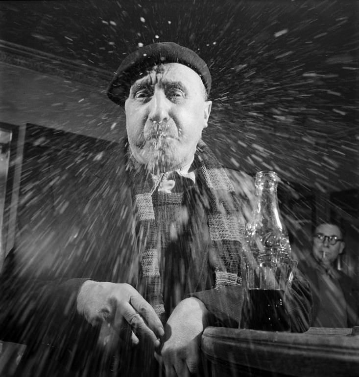 At a Paris bar, a man in a beret spits a mouthful of Coca-Cola at the camera.