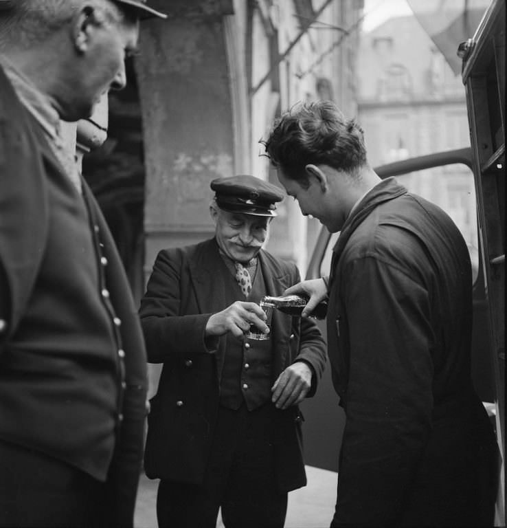 A bystander watches as a man pours a bottle of Coca-Cola into a glass held by a smiling, elderly man, in Paris, France.