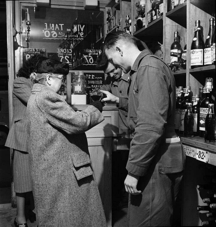 In a Paris shop, a man pours a bottle of Coca-Cola into a glass held by an elderly woman.