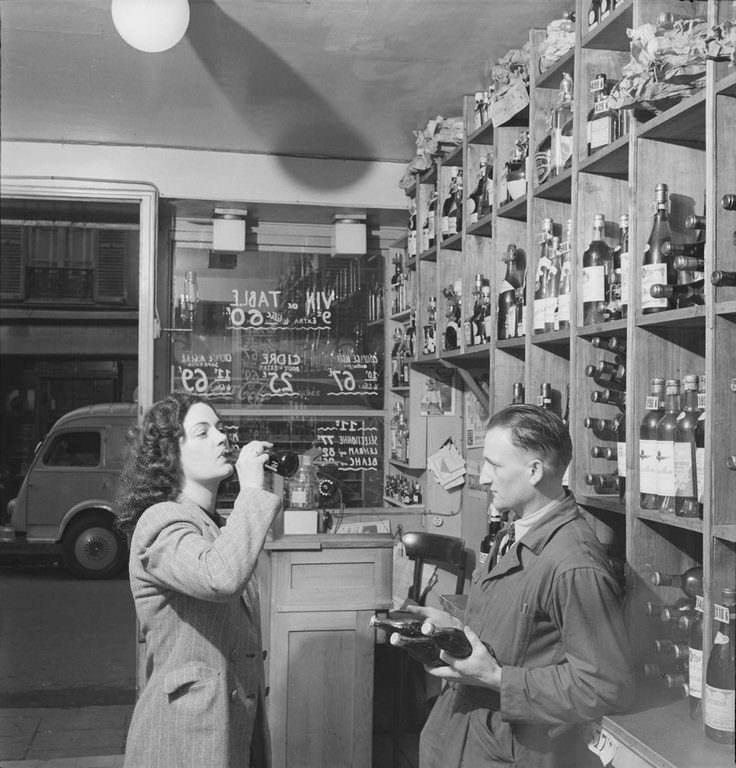 Watched by a man with several bottles in his hands, a woman drinks a bottle of Coca-Cola in a shop, in Paris, France.