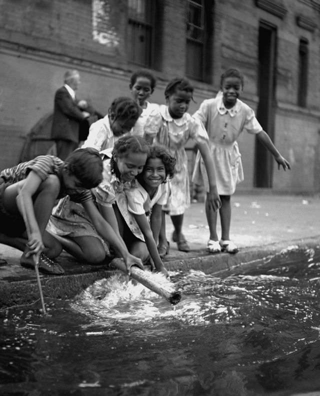 Young girls play beside a flooded street drain, 1947.
