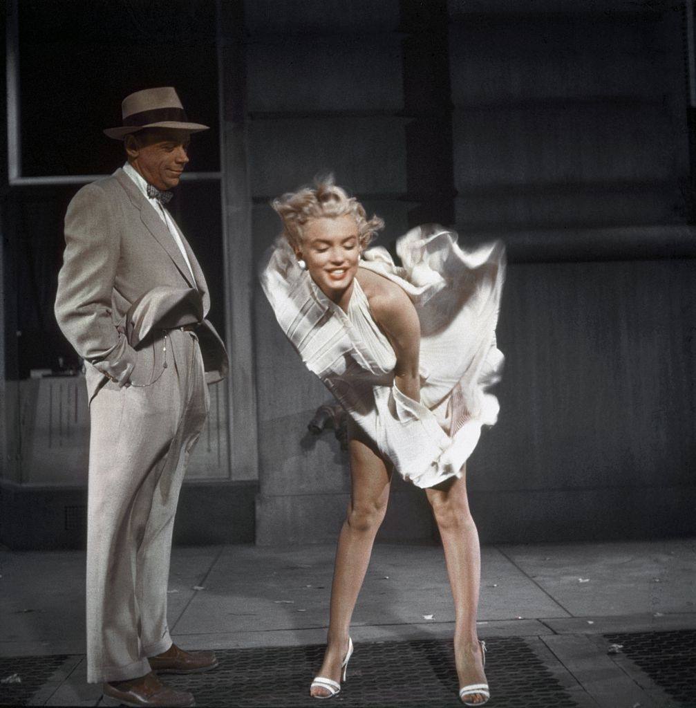 Marilyn Monroe standing over a subway grate with her white dress blowing and co-star Tom Ewell looking on during the filming of "The Seven Year Itch", 1954.