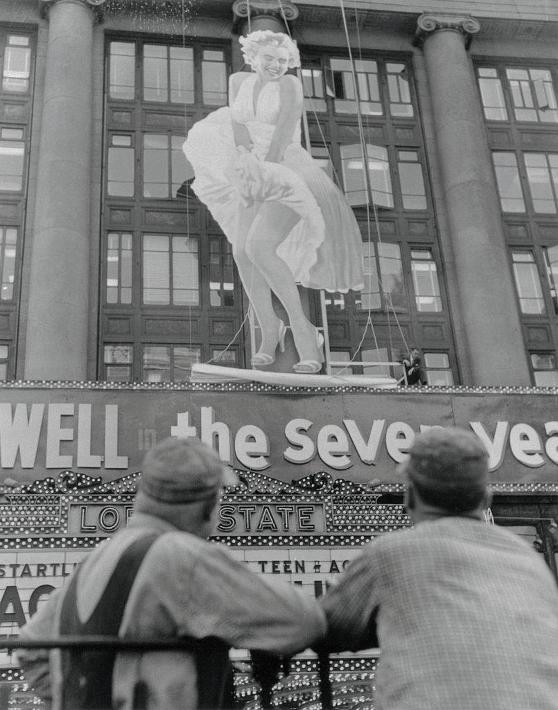 Spectators gawk in Times Square as a fifty-two-foot figure of Marilyn Monroe is erected on the front of Loew's State Theatre.