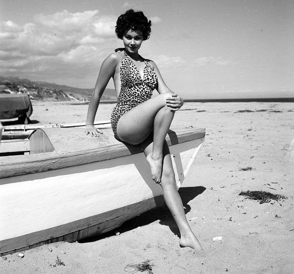 Marla English poseing with a boat at the beach, 1954.