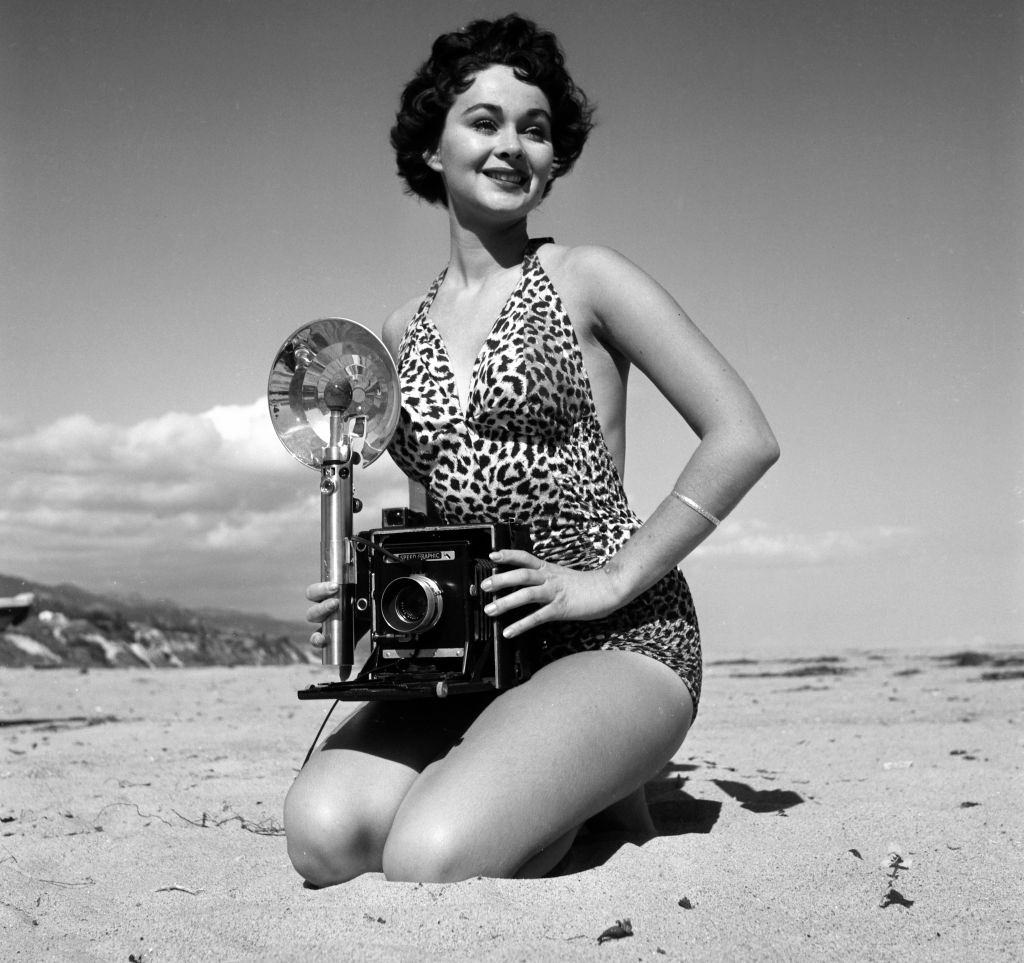 Marla English holding a camera at Los Angeles beach, 1954.