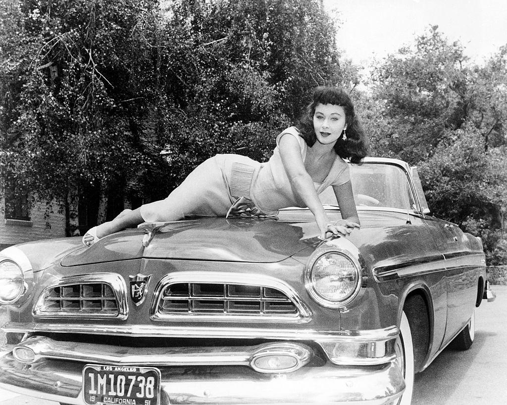 Marla English posing on the bonnet of a convertible car, circa 1955.