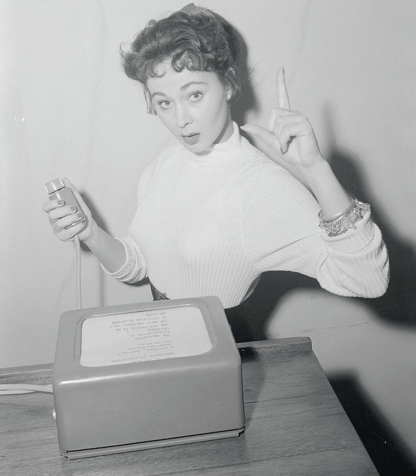 Marla English supplies the gestures as she reads a speech from a machine, 1955.