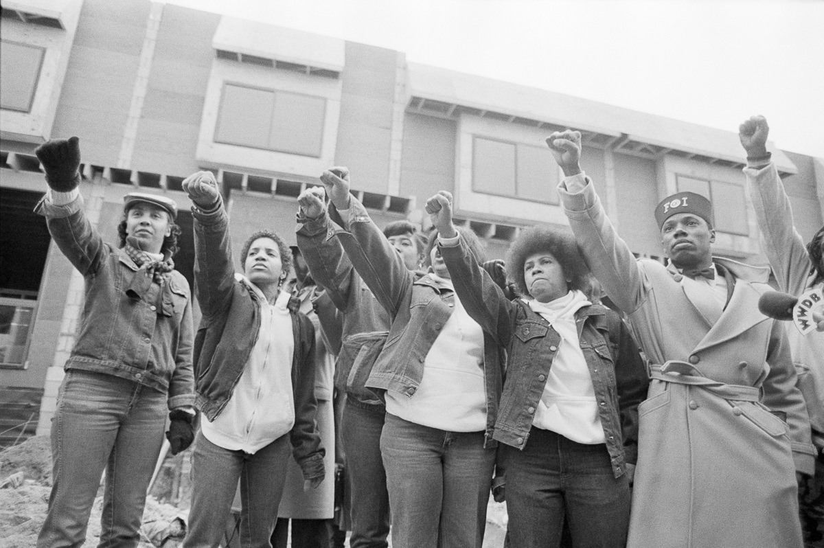 Mourners stand in front of the former MOVE headquarters as the funeral procession of John Africa passes. Dec. 5, 1985