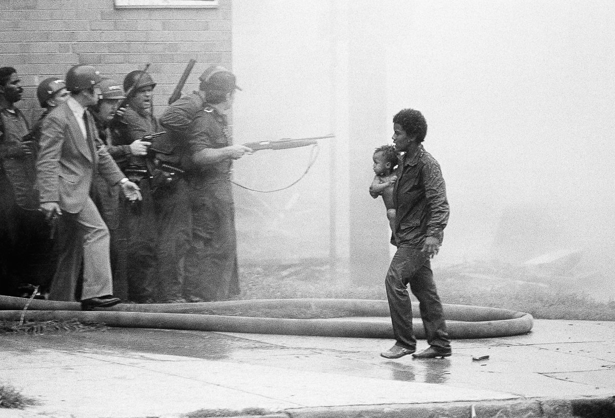 A man flees for safety with a child while police assault the MOVE headquarters. May 13, 1985