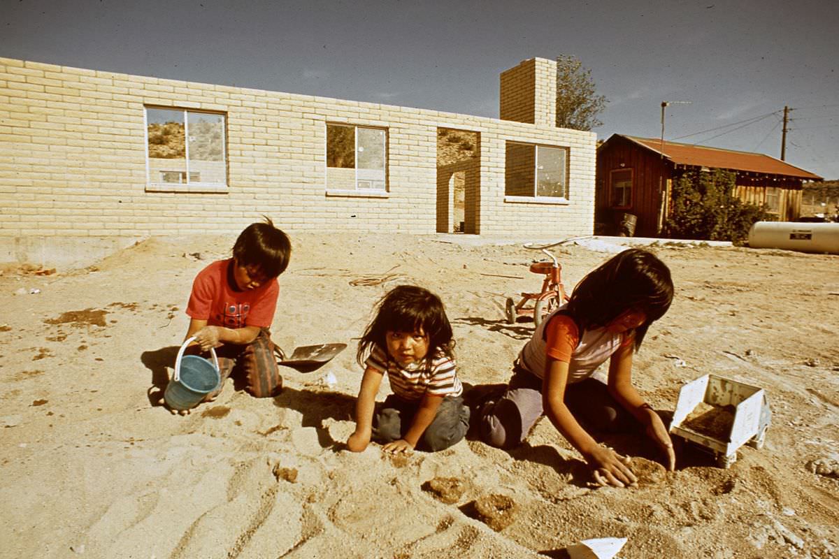 Navajo children play in the sand behind new housing under construction.