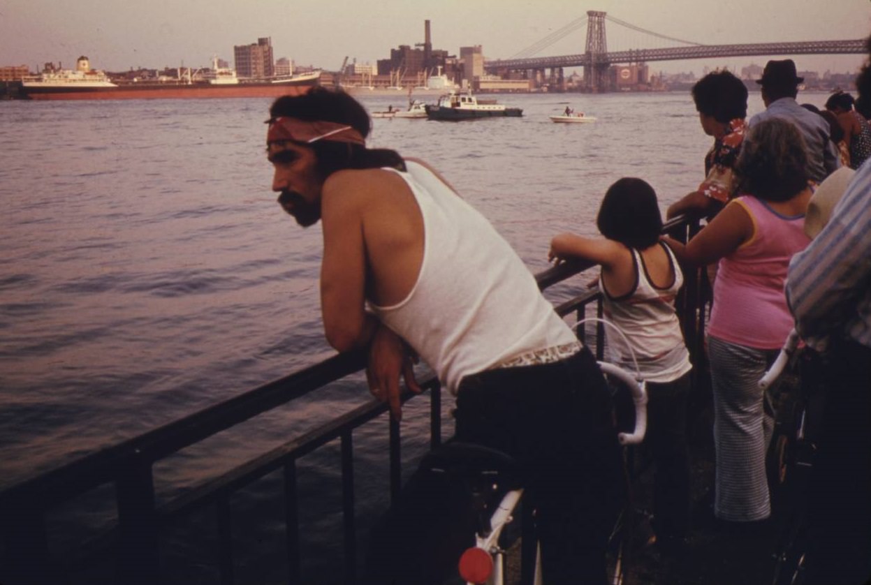 People looking at boat traffic on the East River with the Manhattan Bridge and NYC in the background, July 1974.