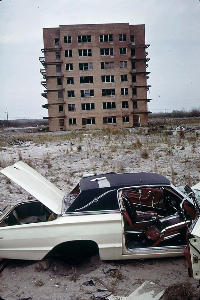 An abandoned 1960s Ford Thunderbird with broken-out windows and a torn vinyl roof, an abandoned apartment building completes the scene, Breezy Point, Queens, June 1973