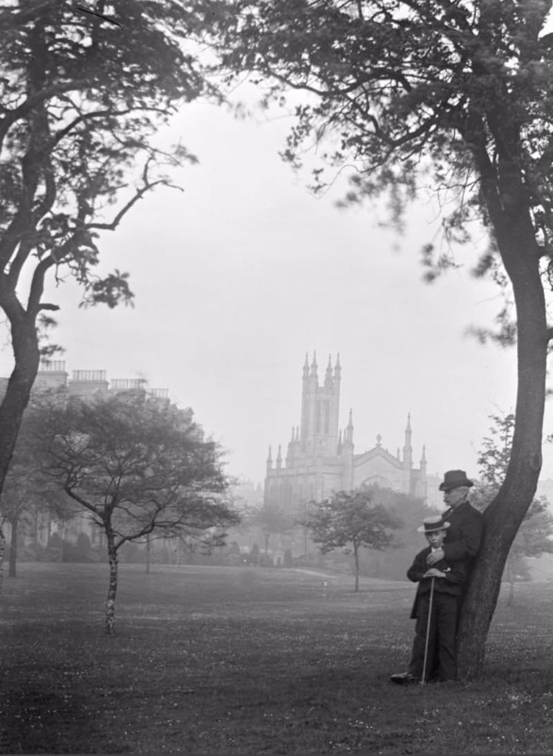 Gentleman and boy leaning on tree with a distant view of Holy Trinity Church, c.1900.