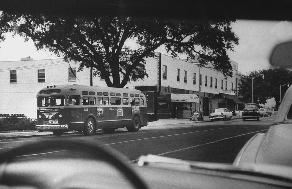 Students sitting on bench watching empty bus go by, 1951.