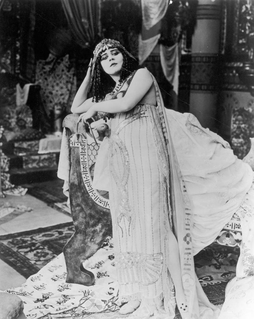 Theda Bara, wearing a costume with entwined sequined snakes and a headdress, 1917.