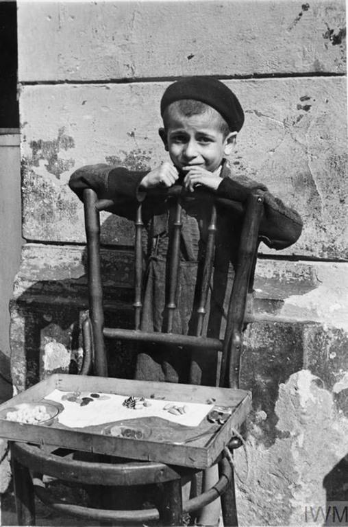 A young boy selling a handful of sweets from a chair in the street.