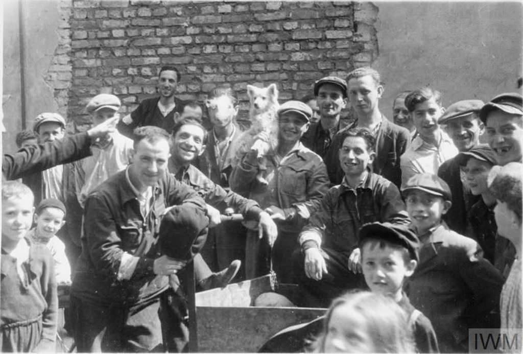 A group of Jewish men and children posing for a photograph in the street of the ghetto. Note the man in the middle, holding a dog on his shoulder.