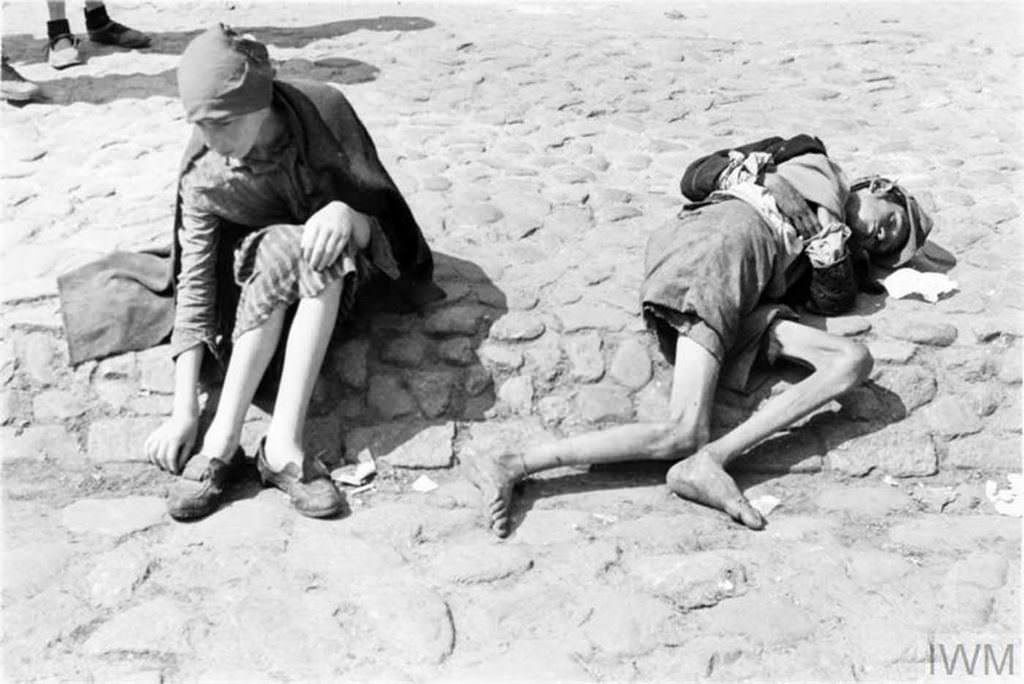 Two emaciated children, one of them asleep or unconscious, begging on the street of the ghetto.