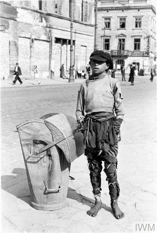 A teenage boy in ragged clothes standing by a waste container (produced by the Silesia Steelworks in Rybnik) in the ghetto.
