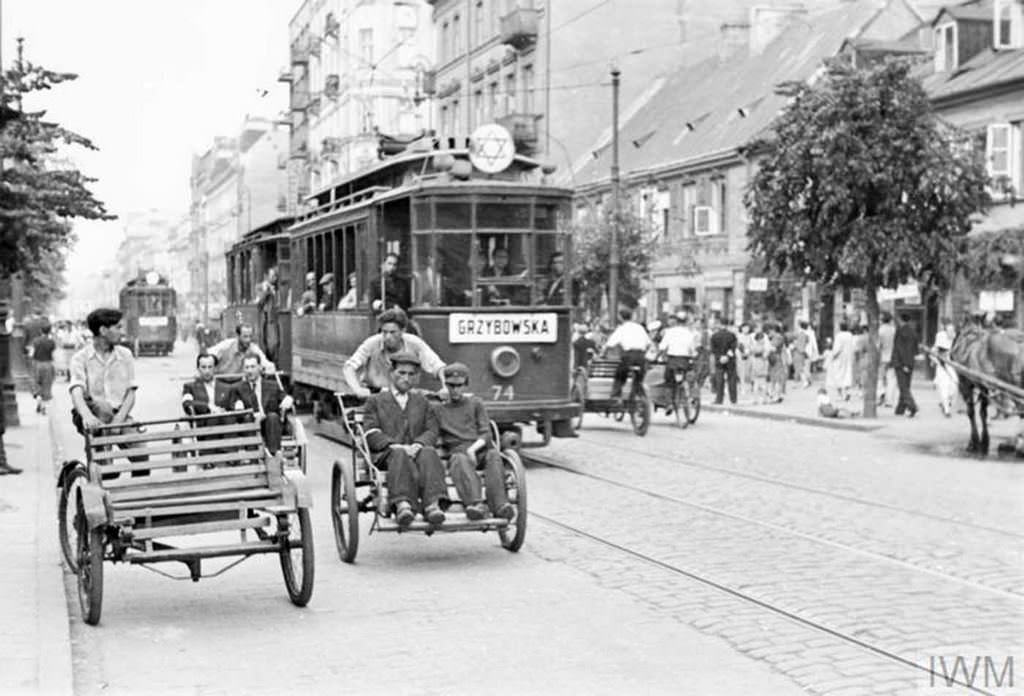Street rickshaws and a tramcar carrying passengers along Leszno Street in the ghetto, summer 1941. This particular tramline was run between the Muranowski Square and the Grzybowska Street. The plaque on the tram indicates it runs towards Grzybowska Street.