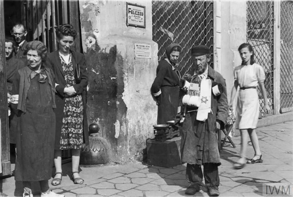 A street armband seller and a group of pedestrians on 18 Zamenhofa Street (probably) in the ghetto, summer 1941. Note two advertising plaques on the wall in the background – for Senior Medic (starszy felczer) named J. Singer and for typewriting services (address given – 18 Zamenhofa Street, flat no.