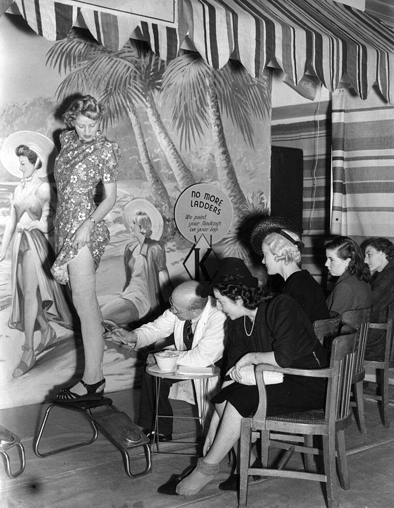 A shoe store offering a service by painting stockings on women's legs during the clothing rationing of World War II.