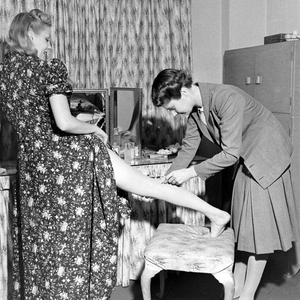 A woman helping another woman with the liquid stockings during WWII