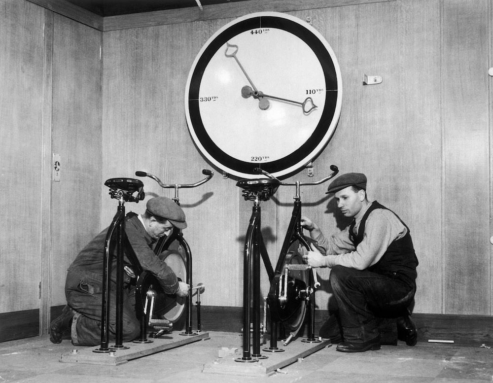 At the time of the installation of the English liner Queen Mary, workmen in the gymnasium of the ship are setting up exercise bikes, with an enormous meter indicating the distance covered. 1932