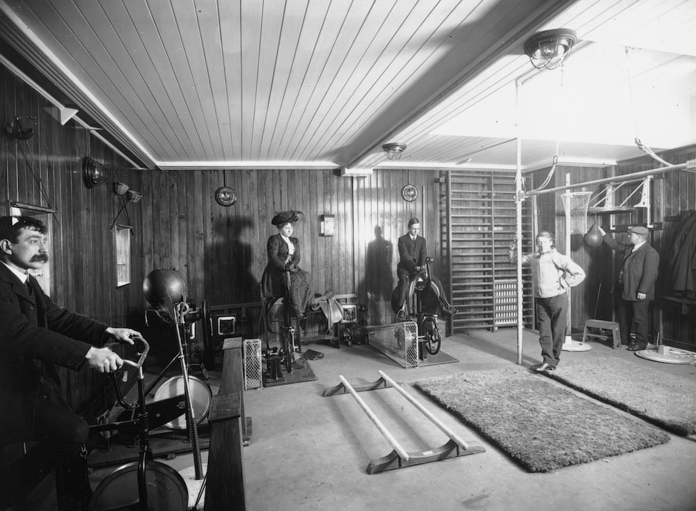 Edwardians riding exercise bikes whilst wearing day clothes in a gymnasium on board the Cunard line liner, RMS Franconia.Feb. 21, 1911