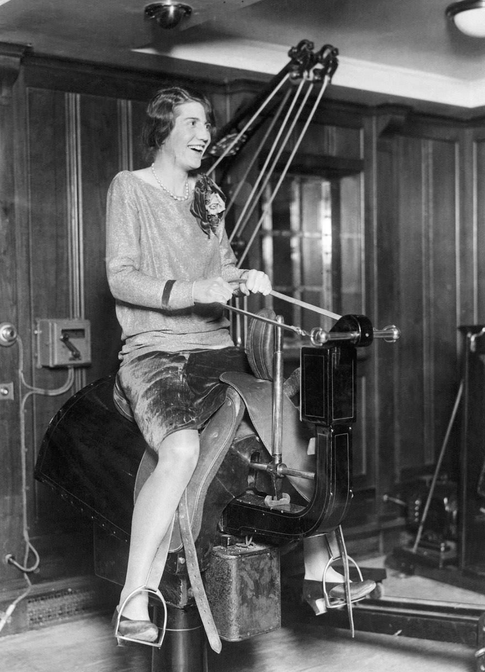 A young woman passenger riding the electric horse in the gym on the liner SS Bermuda. Mid 1920s