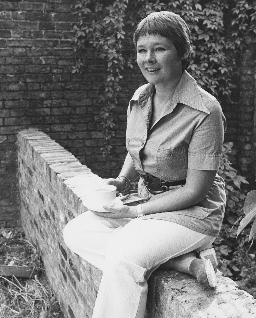 Judi Dench sitting on a brick wall outside her home in Hampstead, 1973.
