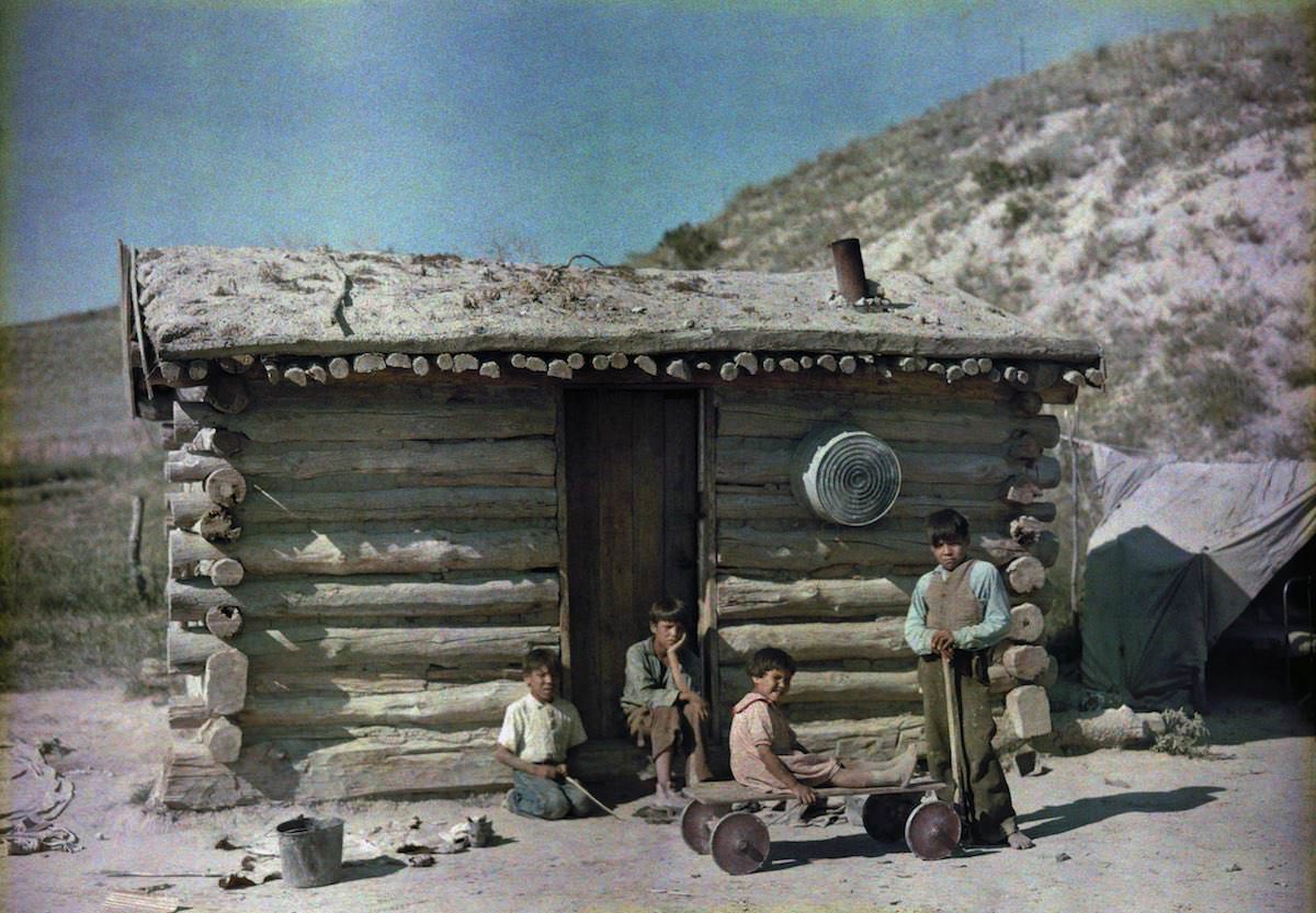 Kids outside a house with a turf roof. Pine Ridge Indian Reservation, South Dakota.