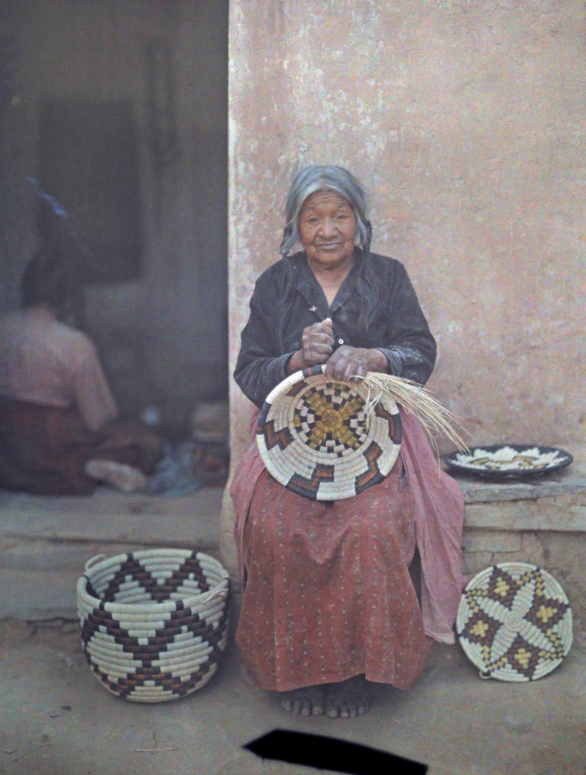 Portrait of a Hopi Indian woman weaving a basket.