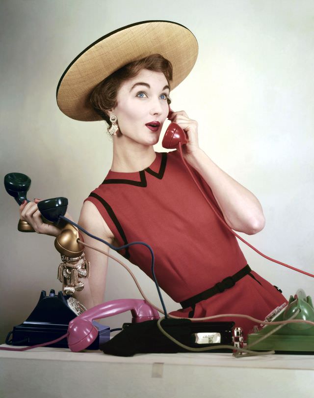 Evelyn Tripp wearing red sleeveless linen dress by Larry Aldrich, and black-rimmed straw boater, Vogue, April 1953