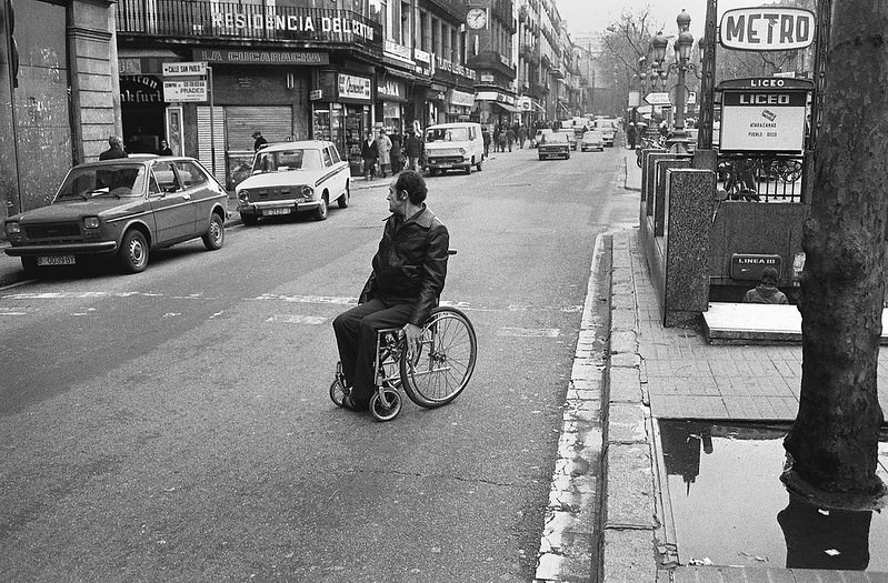 A man in a wheelchair crosses the side road of Las Ramblas, near the Plà de l'Òs. Barcelona, 1979.