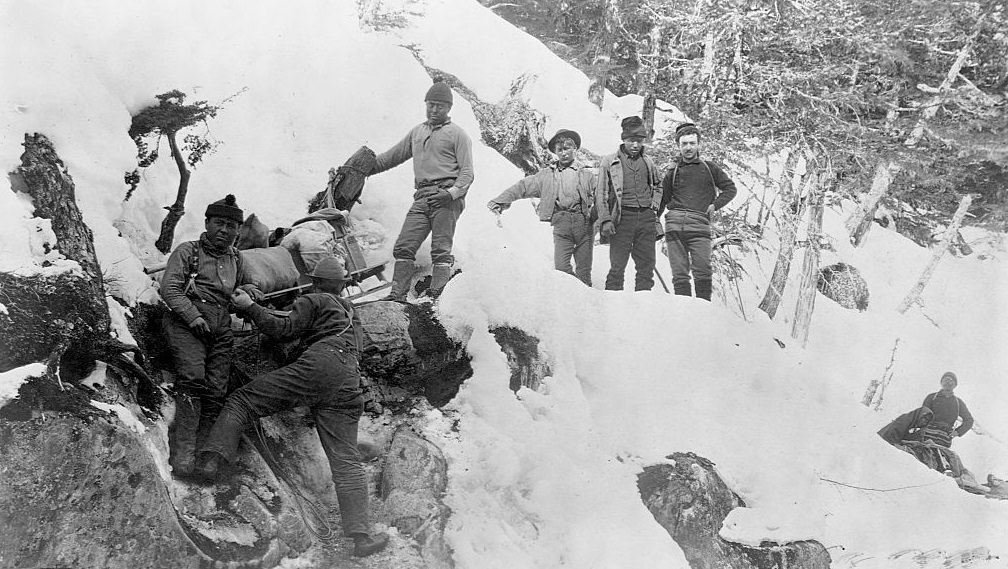 Eight men haul their eguipment up the snow covered Devil's Bluff near Sheep Camp, Alaska, 1895.