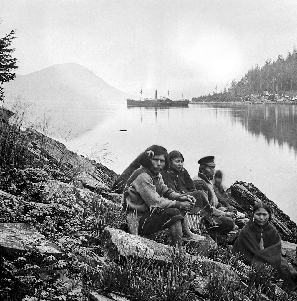 Amerindian family sitting beside a waterway, Alaska, 1868.