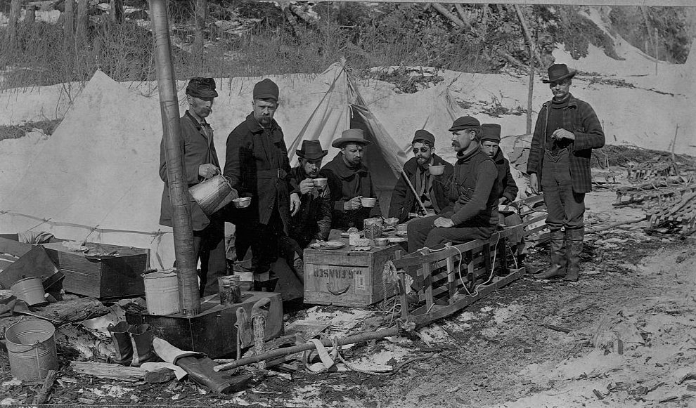 A group of prospectors eat lunch on a crate, on the Yukon Trail. Alaska, 1897.