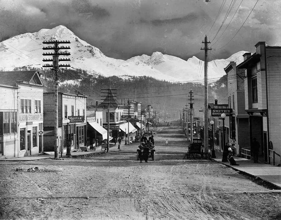 A main street in Cordova, Alaska, with utility poles, boardwalks, and light traffic, 1868.