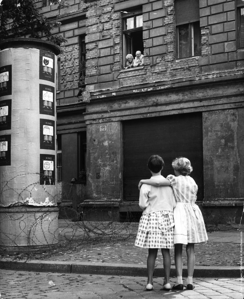 Two little girls in a West German street chat with their grandparents in the window of their home in the eastern zone, separated only by a barbed wire barricade, 14th August 1961.