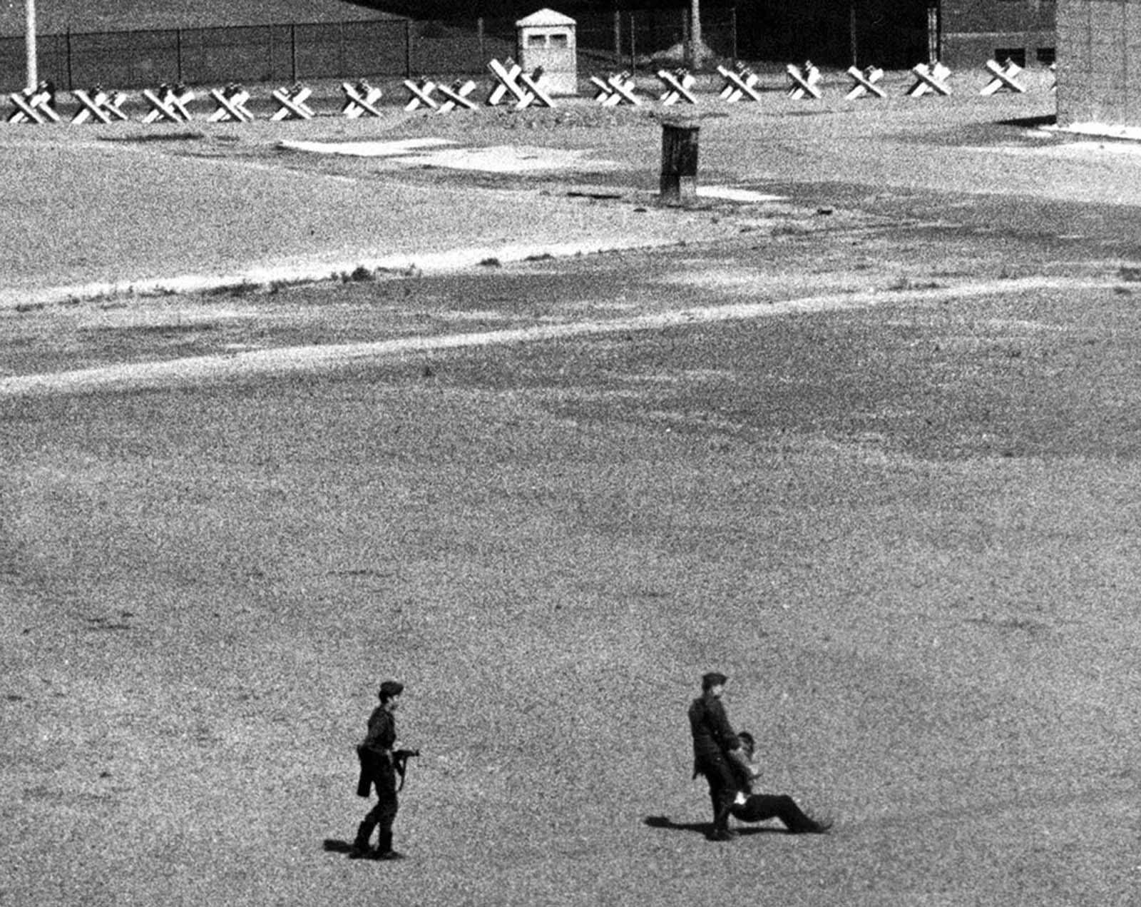 East German border guards carry away a refugee who was wounded by East German machine-gun fire as he dashed through Communist border installations toward the Berlin Wall in 1971.