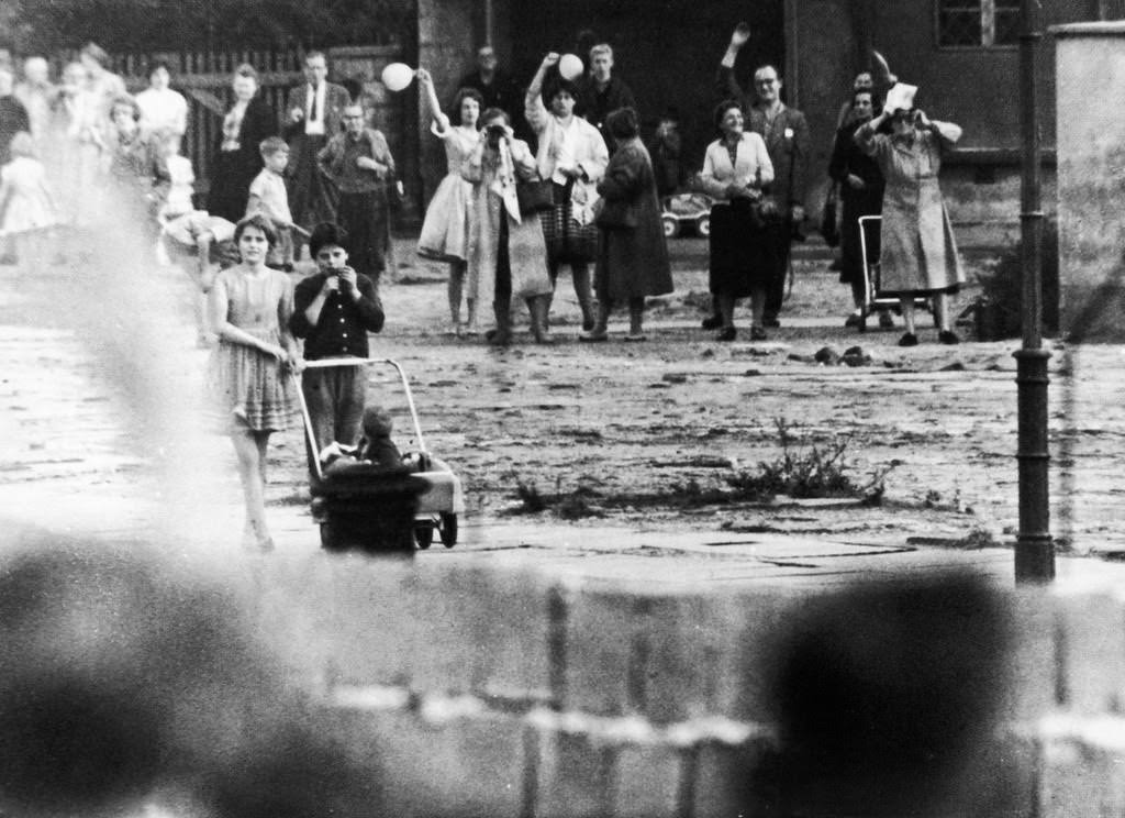 Families and friends, once neighbors, now stand divided and wave across to each other over the Berlin wall.