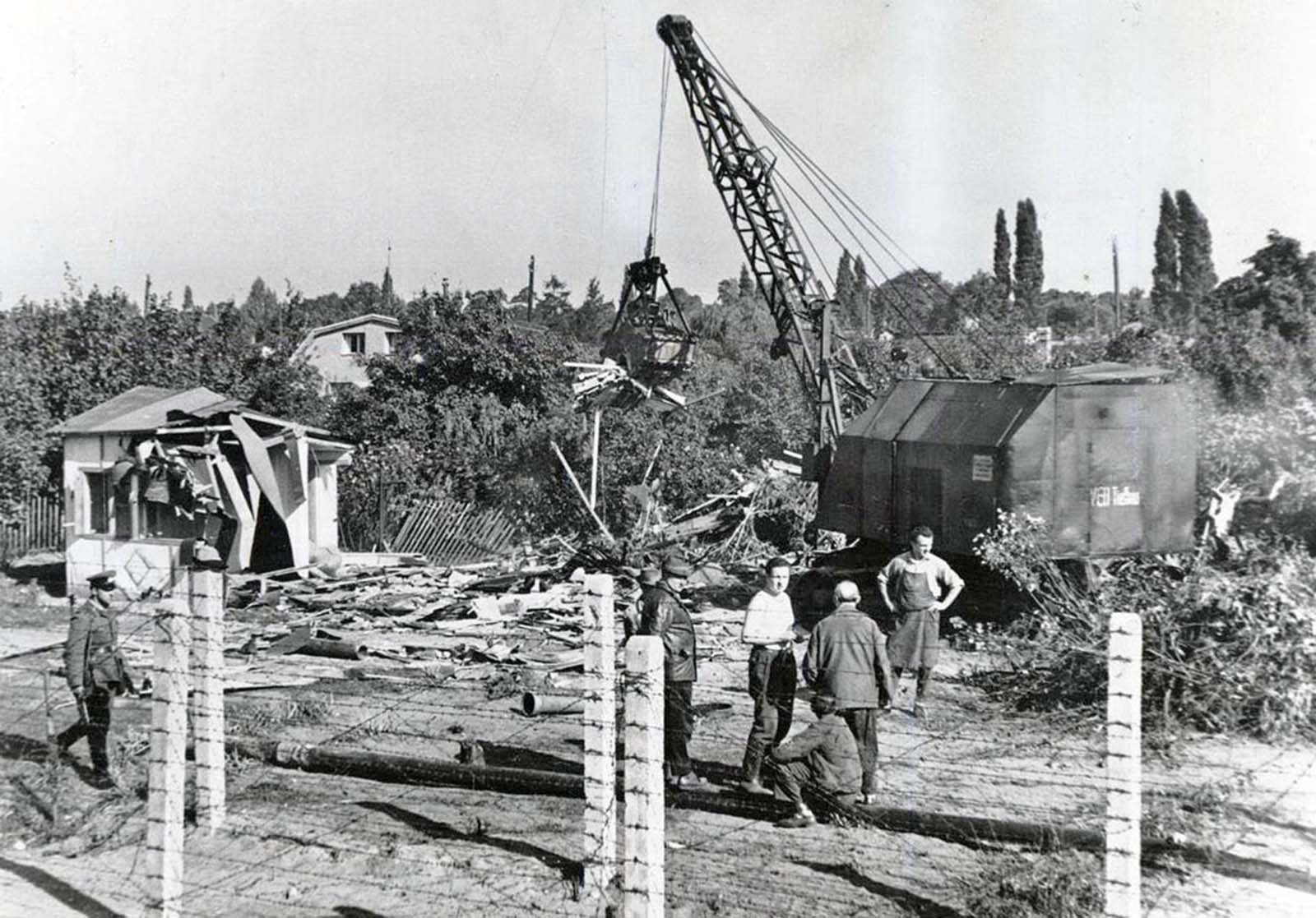 East Berlin workers with a power shovel destroy one of a number of cottages and single-family houses along a sparsely settled stretch of the east-west Berlin boundary in October 1961.