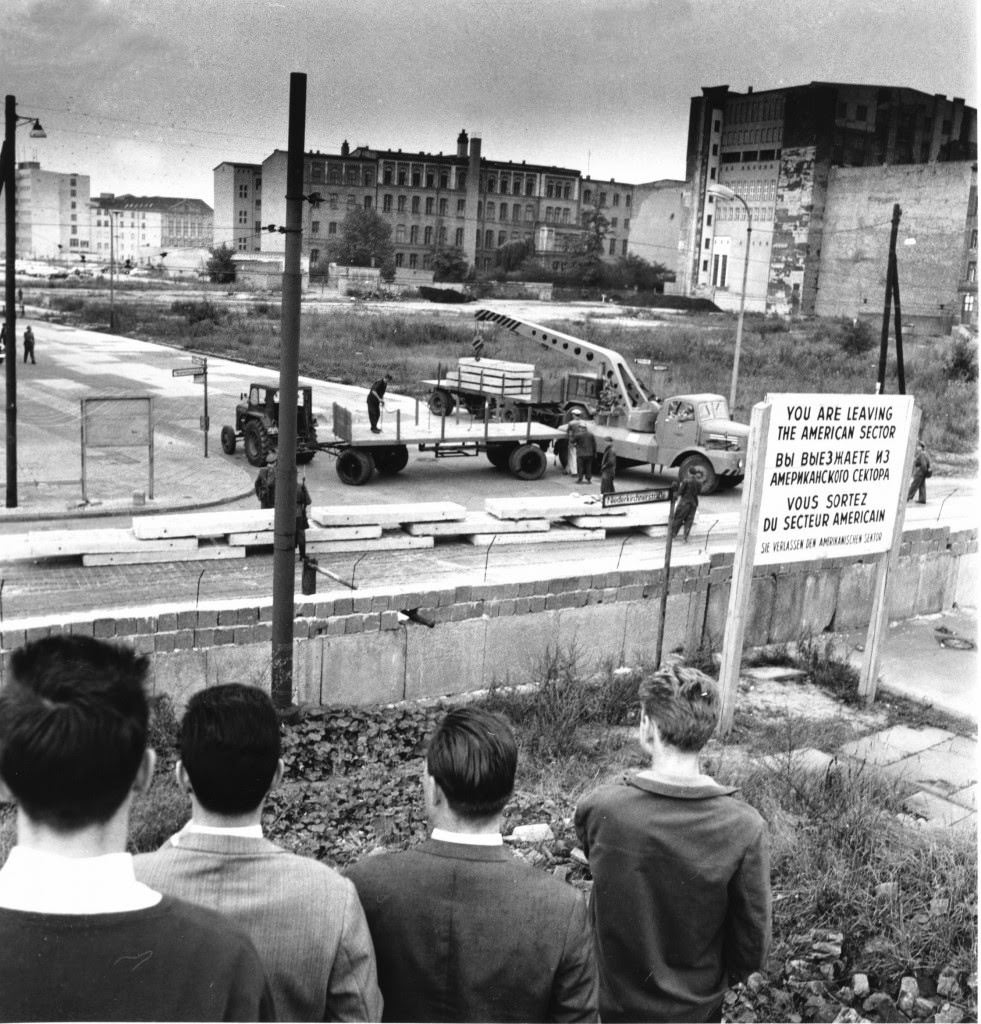West Berliners, with their backs to camera, watch East Berliners unload prefabricated concrete plates to reinforce the Berlin Wall at Wilhelm St. in Berlin, Germany on Sept. 12, 1961.