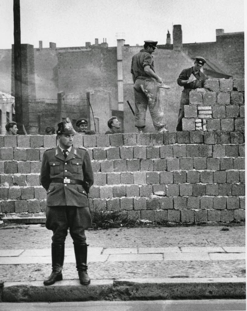 A West Berlin guard stands in front of the concrete wall dividing East and West Berlin at Bernauer Strasse as East Berlin workmen add blocks to the wall to increase the height of the barrier, Oct. 7, 1961.