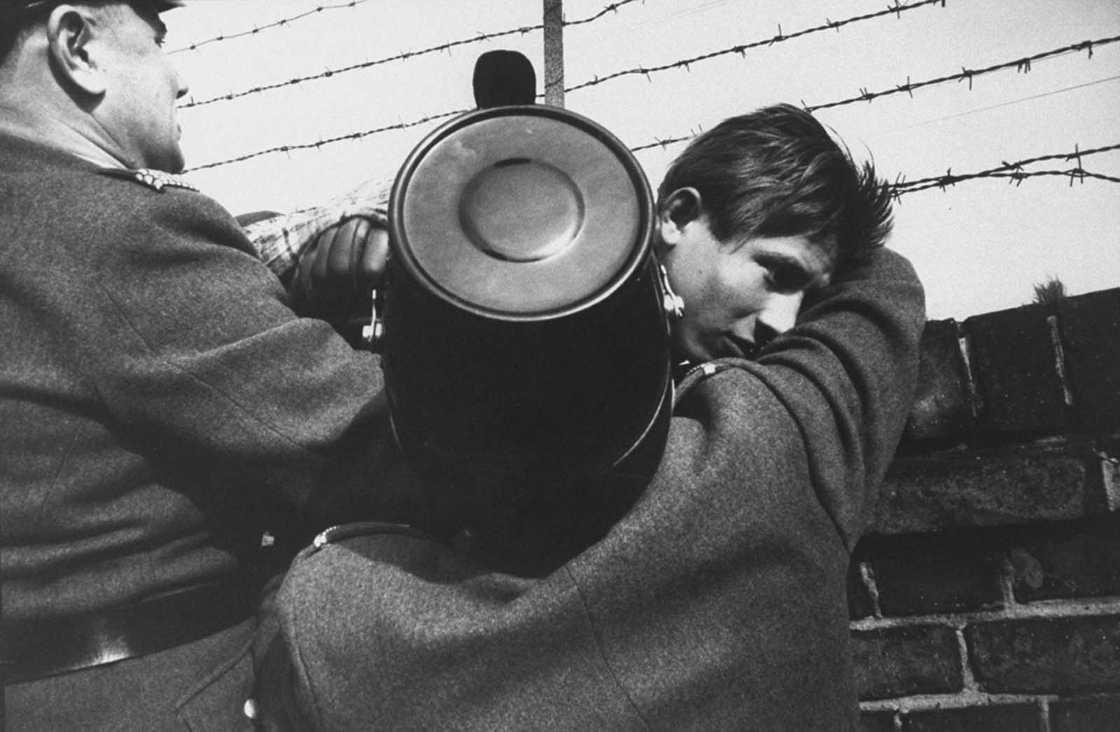 A 17-year-old East Berlin youth is helped down from the Berlin Wall by two friendly West Berlin police officers after he climbed over to freedom in October 1961.